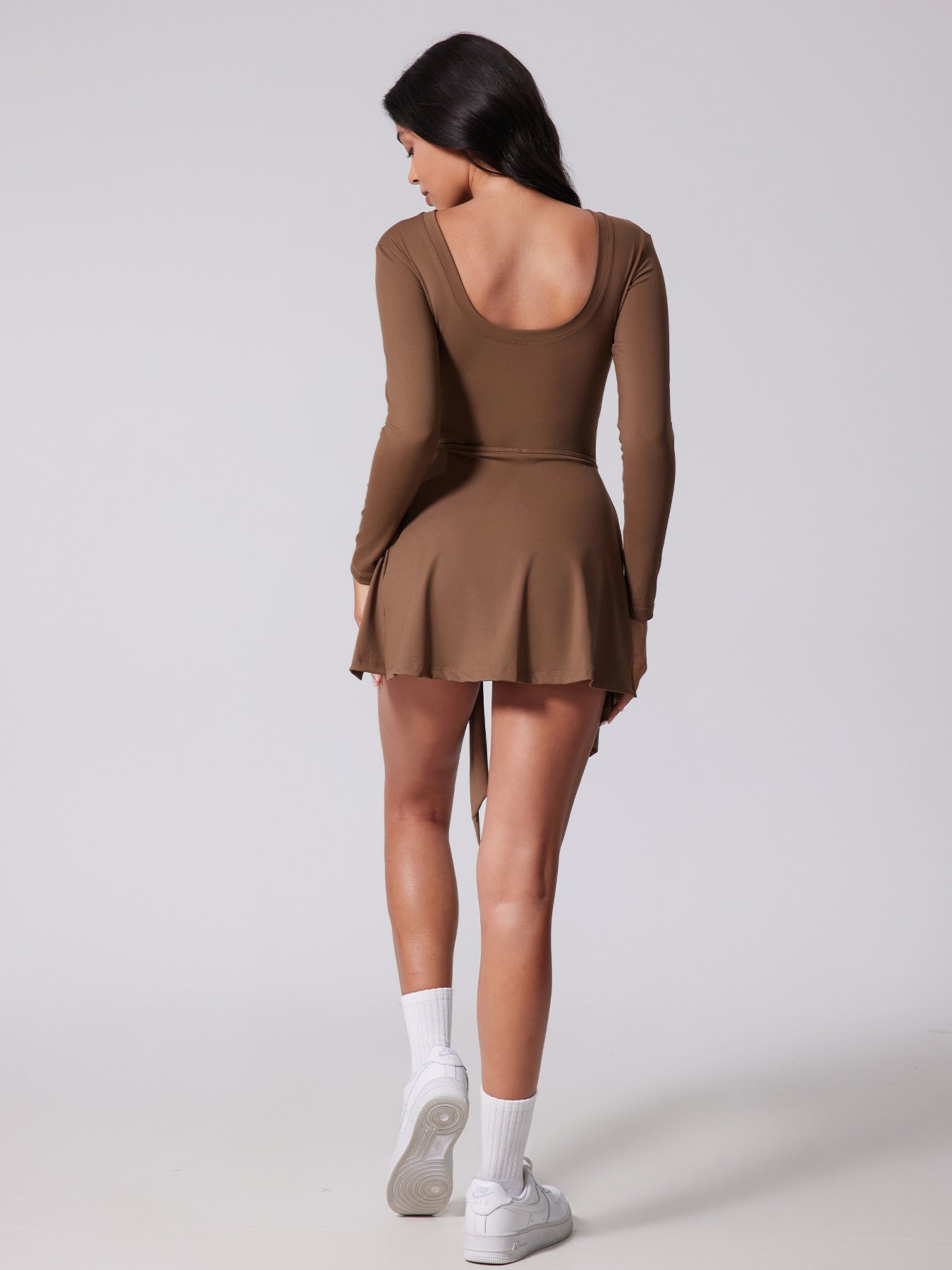 Woman wearing a brown dress with long sleeves and a skirt on a white background